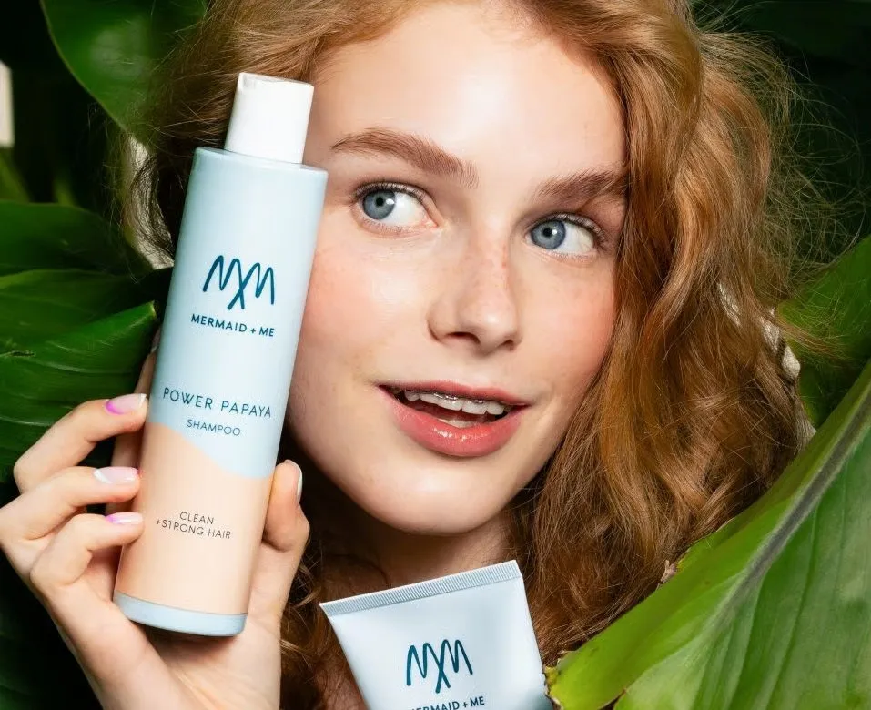 Model holding a Mermaid + Me shampoo among green leaves
